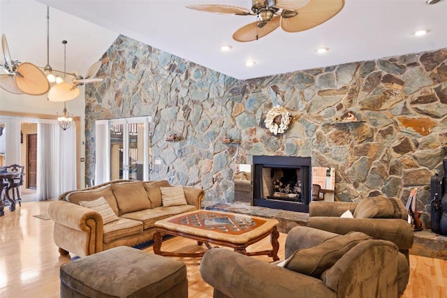 living room with a stone fireplace, light hardwood / wood-style flooring, and ceiling fan with notable chandelier