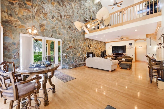 living room featuring a high ceiling, a fireplace, ceiling fan with notable chandelier, and light hardwood / wood-style flooring