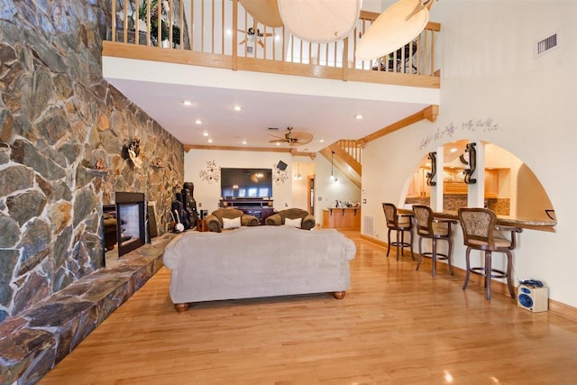 living room with a towering ceiling, ceiling fan, light wood-type flooring, and a fireplace