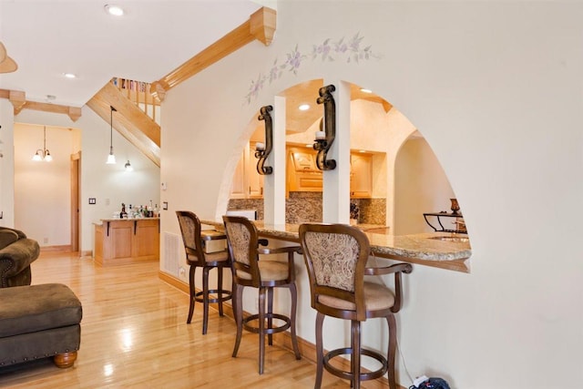 kitchen with kitchen peninsula, stone countertops, a breakfast bar, light hardwood / wood-style flooring, and pendant lighting