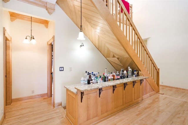 bar with light stone countertops, hanging light fixtures, an inviting chandelier, light hardwood / wood-style floors, and beam ceiling