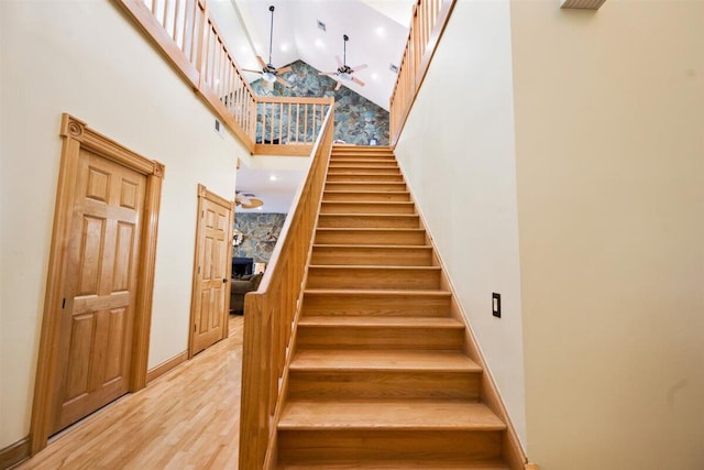 stairway featuring a high ceiling, ceiling fan, and light wood-type flooring