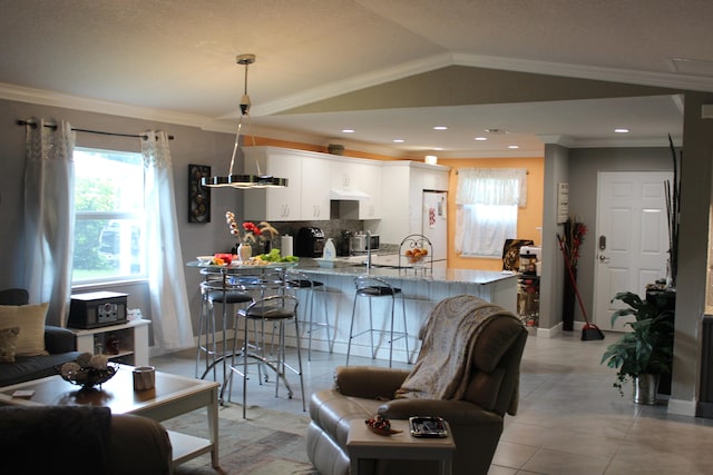 kitchen with decorative light fixtures, light tile floors, white cabinets, vaulted ceiling, and ornamental molding