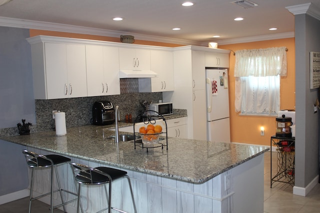 kitchen featuring kitchen peninsula, white fridge, dark stone countertops, premium range hood, and white cabinetry