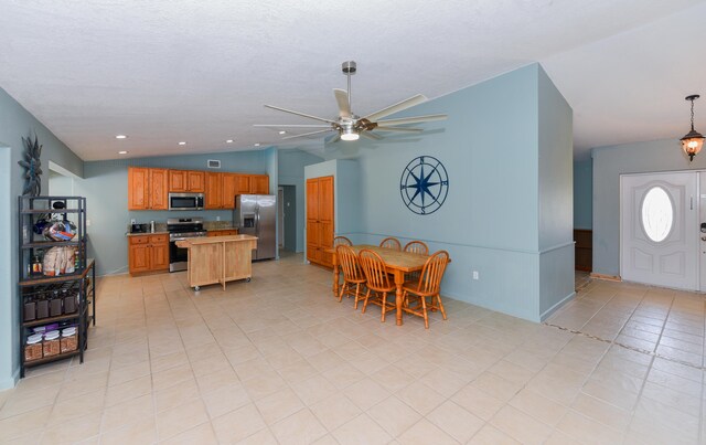 kitchen with lofted ceiling, pendant lighting, ceiling fan, appliances with stainless steel finishes, and a center island