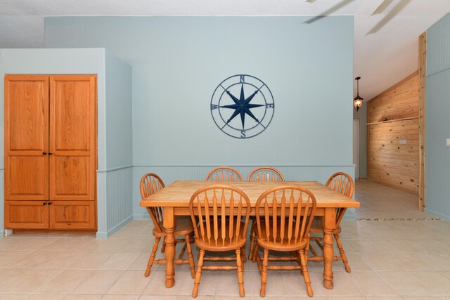 tiled dining room featuring vaulted ceiling and wooden walls