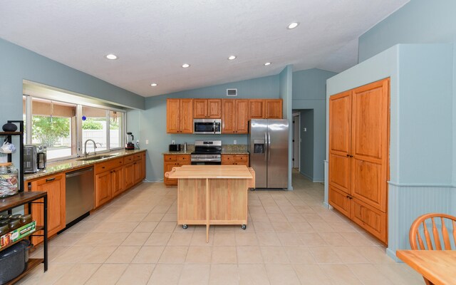 kitchen featuring sink, vaulted ceiling, a kitchen island, stainless steel appliances, and light stone countertops