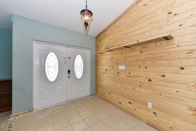 foyer featuring vaulted ceiling, light tile patterned floors, and wood walls