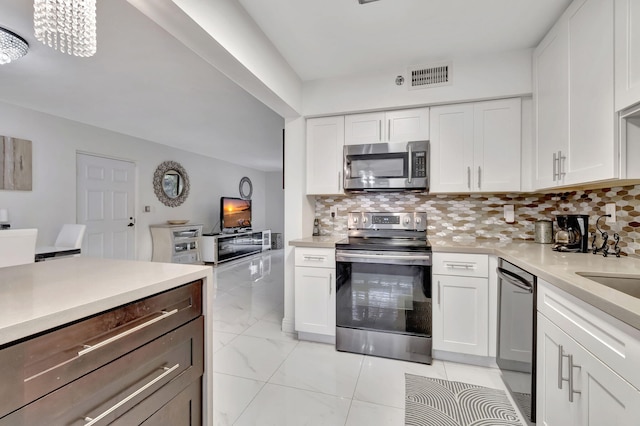 kitchen featuring white cabinetry, backsplash, appliances with stainless steel finishes, and an inviting chandelier