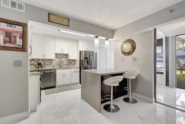 kitchen with decorative backsplash, appliances with stainless steel finishes, a kitchen breakfast bar, a center island, and white cabinetry