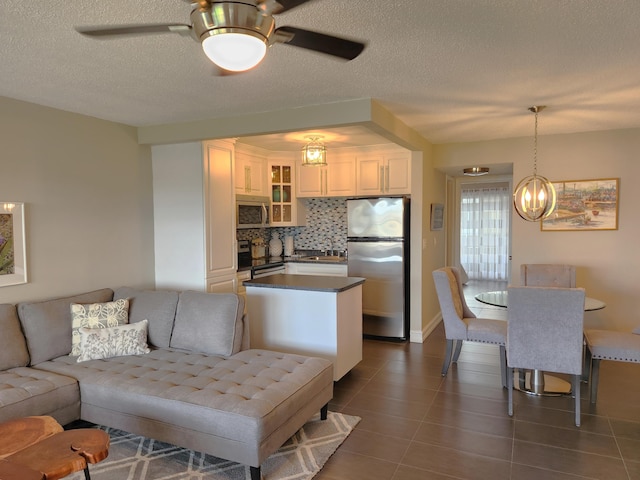 living room featuring a textured ceiling, ceiling fan with notable chandelier, and dark tile floors