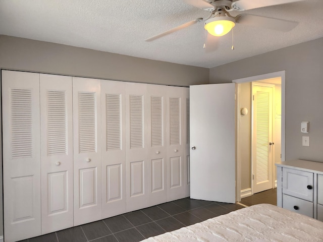 unfurnished bedroom with dark tile floors, ceiling fan, a textured ceiling, and a closet