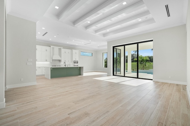 unfurnished living room with sink, a tray ceiling, and crown molding