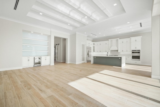 unfurnished living room featuring a barn door, wine cooler, a tray ceiling, sink, and light hardwood / wood-style flooring