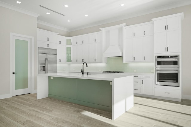 kitchen with sink, a kitchen island with sink, premium range hood, and appliances with stainless steel finishes