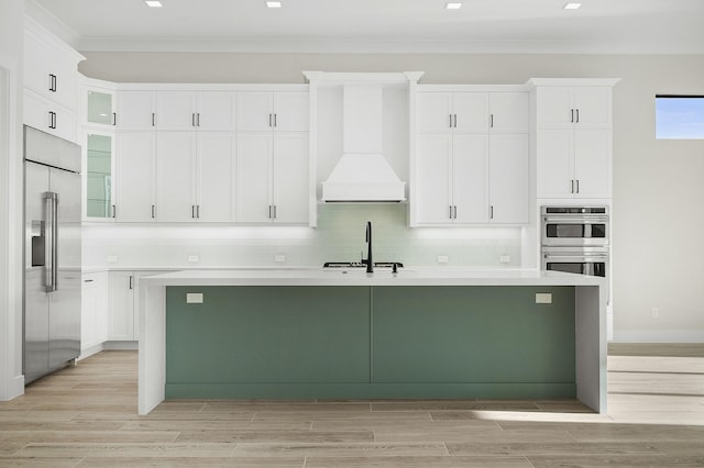 kitchen with white cabinetry, a kitchen island with sink, premium range hood, and appliances with stainless steel finishes