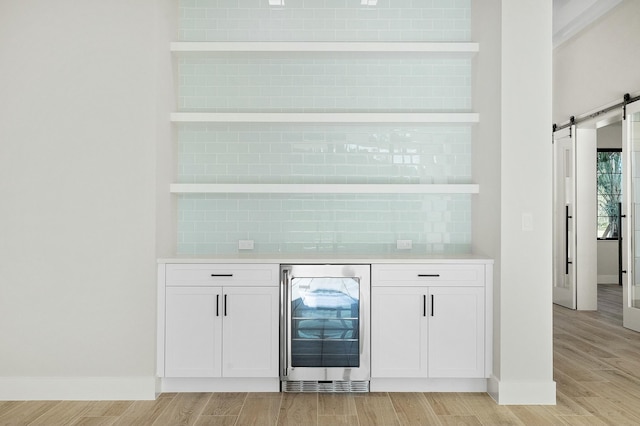 bar with white cabinets, light wood-type flooring, a barn door, and wine cooler