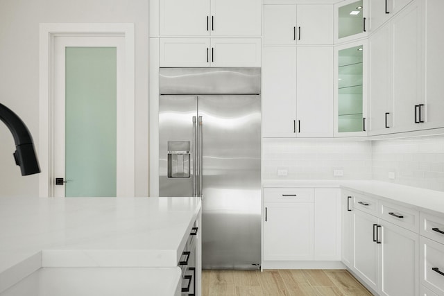 kitchen featuring light hardwood / wood-style flooring, built in refrigerator, white cabinetry, and backsplash