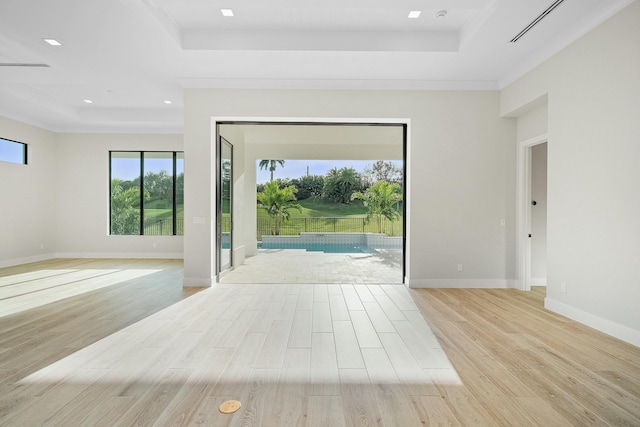 empty room featuring a raised ceiling, ornamental molding, and light hardwood / wood-style flooring