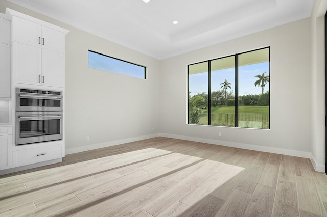 kitchen featuring double oven, a raised ceiling, light wood-type flooring, and white cabinetry