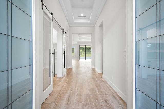 corridor with a raised ceiling, a barn door, and light hardwood / wood-style floors