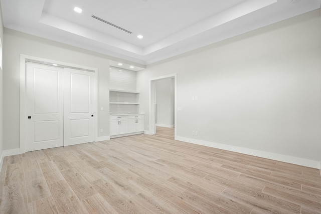 unfurnished bedroom featuring a tray ceiling and light hardwood / wood-style flooring