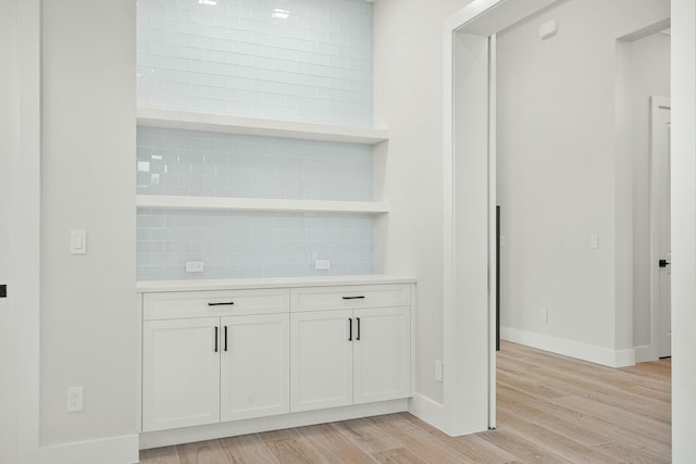 bar with light hardwood / wood-style floors, white cabinetry, and tasteful backsplash