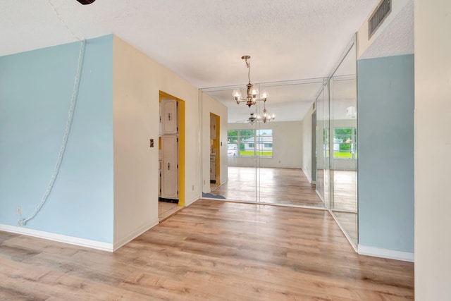 hallway with a chandelier, a textured ceiling, and light hardwood / wood-style flooring