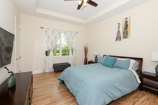 bedroom with ceiling fan, light hardwood / wood-style floors, and a raised ceiling