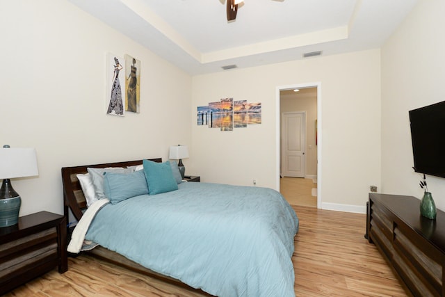 bedroom with a raised ceiling, ceiling fan, and light wood-type flooring