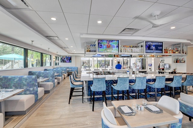 bar with light stone counters, a wealth of natural light, a drop ceiling, and light hardwood / wood-style flooring