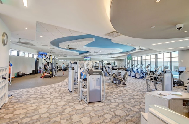 gym featuring light colored carpet, ceiling fan, and a tray ceiling