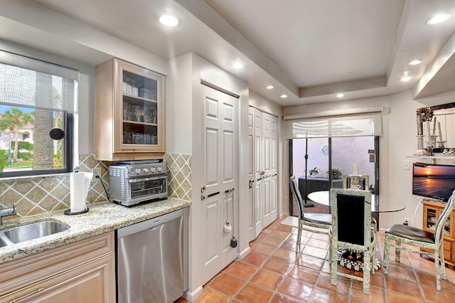 kitchen featuring tasteful backsplash, dishwasher, light stone counters, and a tray ceiling