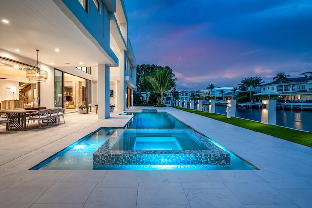 pool at dusk with a residential view, a pool with connected hot tub, a patio, and a water view