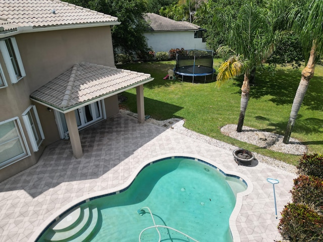 view of pool with a trampoline, a yard, and a patio