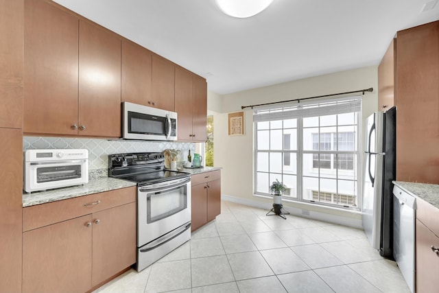 kitchen with backsplash, light stone countertops, light tile floors, and appliances with stainless steel finishes