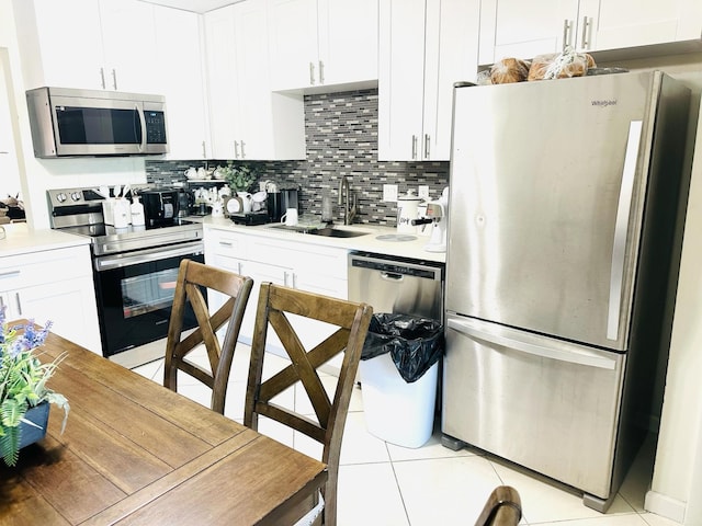 kitchen featuring appliances with stainless steel finishes, backsplash, sink, light tile patterned floors, and white cabinets