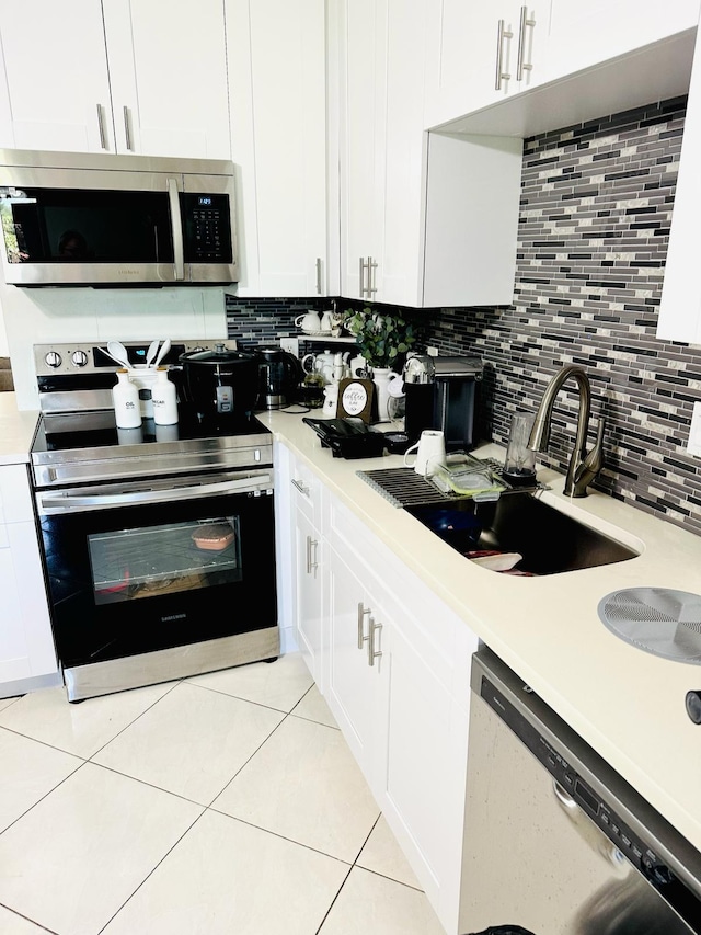 kitchen featuring white cabinets, sink, decorative backsplash, light tile patterned floors, and appliances with stainless steel finishes