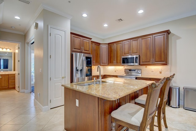 kitchen featuring light stone countertops, backsplash, stainless steel appliances, light tile patterned floors, and an island with sink