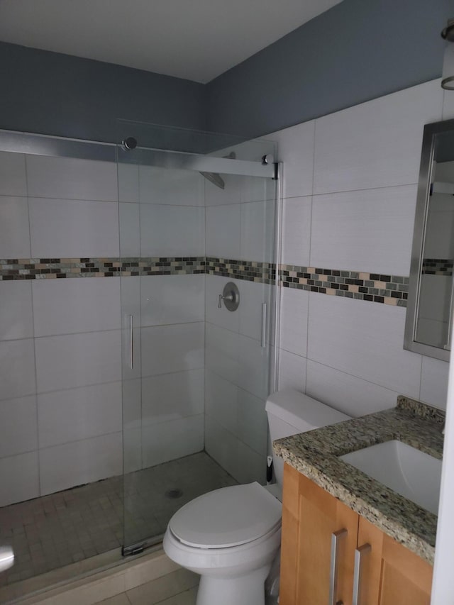 bathroom featuring tile walls, walk in shower, toilet, tile floors, and vanity