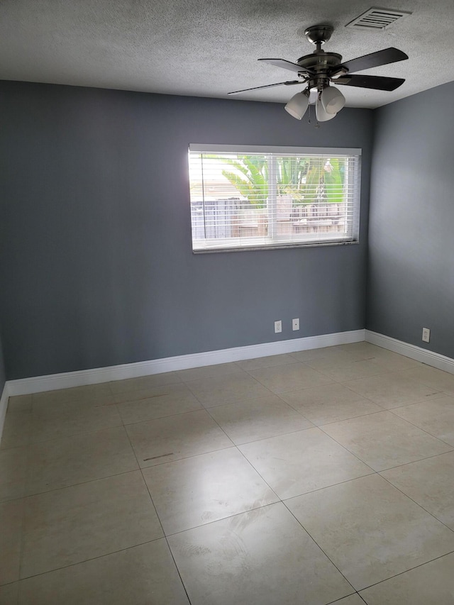 empty room with a textured ceiling, ceiling fan, and light tile flooring