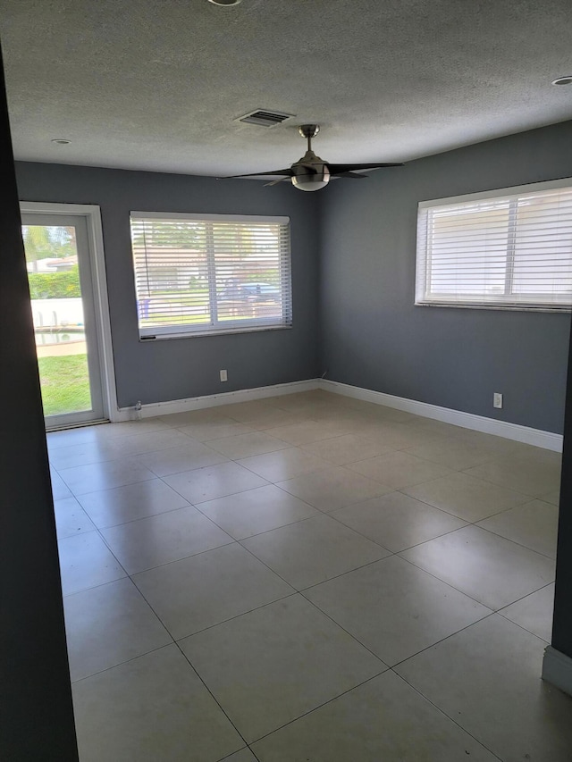 tiled empty room with ceiling fan and a textured ceiling