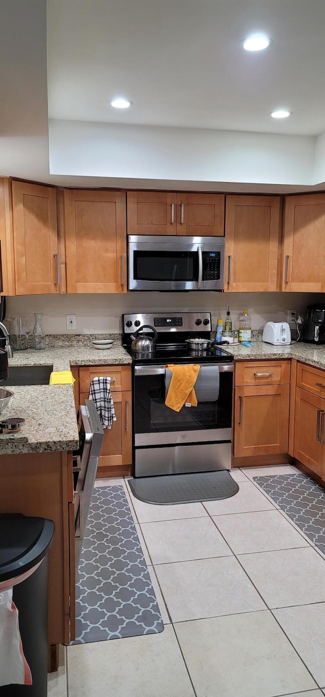 kitchen with light tile flooring, stainless steel appliances, and light stone countertops