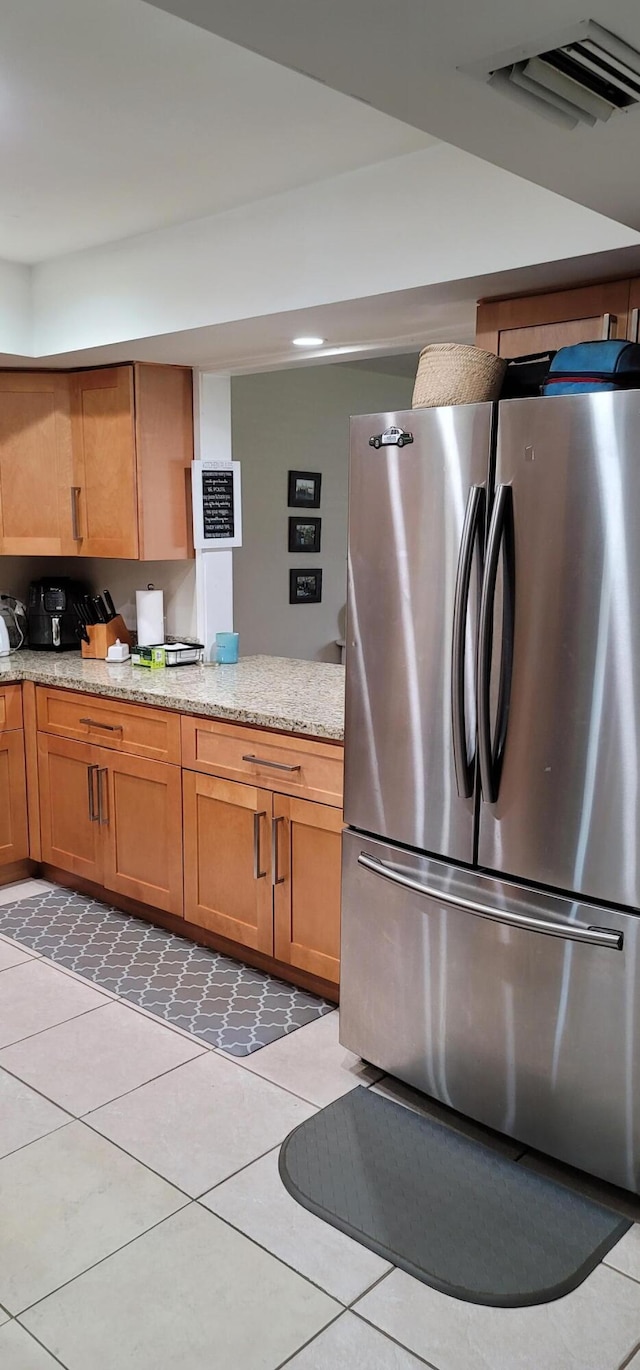 kitchen featuring stainless steel refrigerator, light tile flooring, and light stone counters