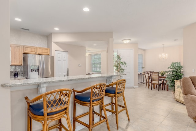 kitchen with light tile flooring, light brown cabinets, a chandelier, stainless steel refrigerator with ice dispenser, and a breakfast bar area