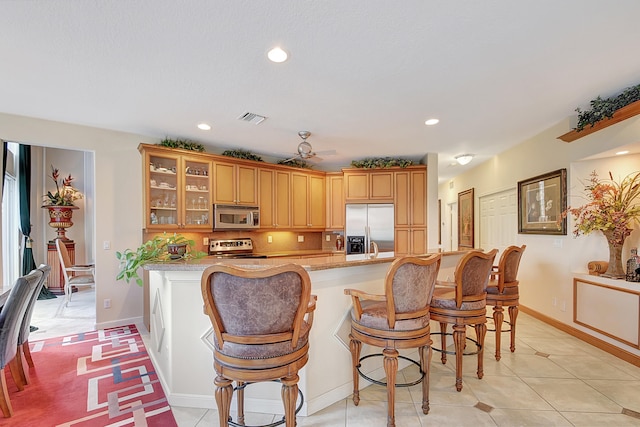 kitchen with a kitchen breakfast bar, kitchen peninsula, light tile patterned floors, and appliances with stainless steel finishes