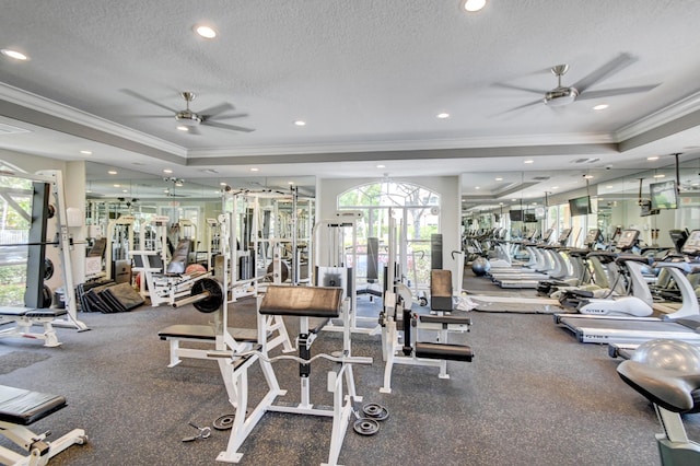 workout area with a tray ceiling, ceiling fan, crown molding, and a textured ceiling