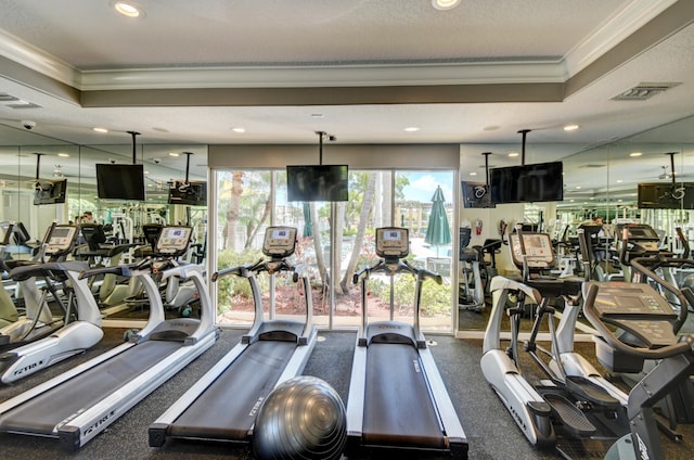 workout area featuring a tray ceiling, crown molding, and a textured ceiling