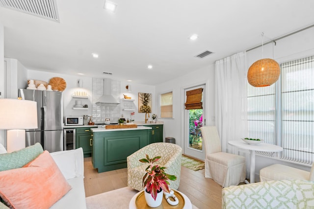 interior space featuring green cabinets, wall chimney exhaust hood, backsplash, stainless steel refrigerator, and light wood-type flooring