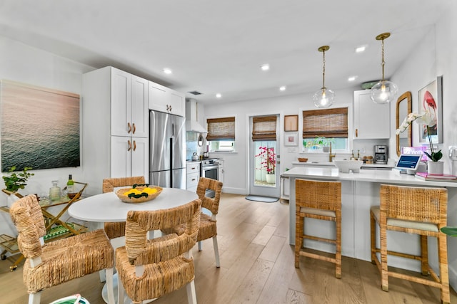 kitchen with hanging light fixtures, white cabinets, appliances with stainless steel finishes, a kitchen bar, and light wood-type flooring